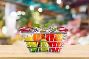 cesta de la compra con frutas en la mesa de madera sobre el fondo borroso del supermercado de la tienda de comestibles foto