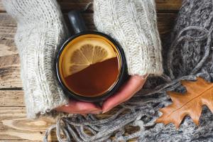Woman's hand holding cup of tea with lemon on a cold day. Wooden table. Top view. Concept autumn photo