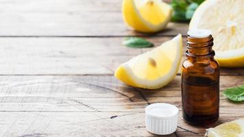 Essential lemon oil in bottle, fresh fruit slices on wooden background. Natural fragrances. photo