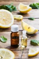 Essential lemon oil in bottle, fresh fruit slices on wooden background. Natural fragrances. photo