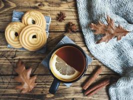 Autumn still life with cup of tea, cookies, sweater and leaves on wooden background. concept of cozy autumn, fall season photo
