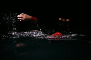 atleta de triatlón nadando en la noche oscura con traje de neopreno foto