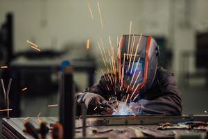 Professional Heavy Industry Welder Working Inside factory, Wears Helmet and Starts Welding. Selective Focus photo