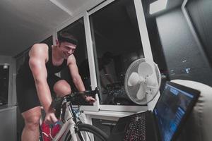 Man cycling on the machine trainer he is exercising in the home at night playing online bike racing game photo