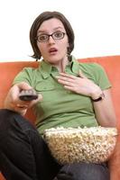 mujer joven come palomitas de maíz y ve la televisión foto