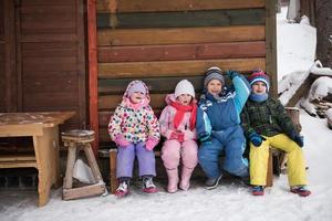 little children group sitting  together  in front of wooden cabin photo