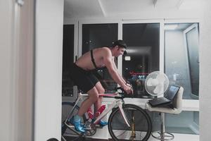 Man cycling on the machine trainer he is exercising in the home at night playing online bike racing game photo