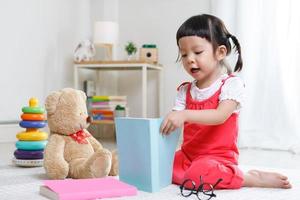 Preschooler girl learns at school. Cute child reading with teddy bear. Little girl having fun indoors at home, kindergarten or photo