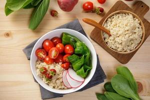 Quinoa salad with vegetables, raspberry and tomatoes on the wooden table. Super food for healthy and concept of balanced diet photo