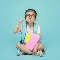 Asian little girl with book thinking and learning, studio shot isolated on colorful blue background, Creative of baby and genius concept photo