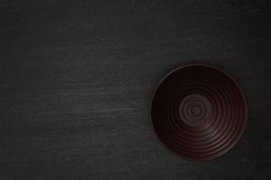 Empty blank brown ceramic round bowl on black stone blackground with copy space, Top view of traditional handcrafted kitchenware concept photo