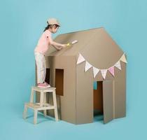 Asian little child girl painting her cardboard house isolated on blue background, Creative at home with family concept photo