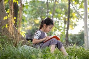 A pretty little Asian girl reading a book under the big tree. photo