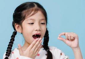 Asian child's hand shows the fallen out small white milk tooth close-up, Dentistry and Health care concept, Empty space isolated on blue background photo