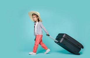 Asian little girl tourist woman with black luggage to travel on weekends, empty space in studio shot isolated on colorful blue background photo