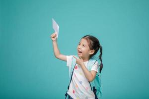 bella niña asiática sonriente señalando la mano, espacio vacío en una foto de estudio aislada en un colorido fondo azul, concepto educativo para la escuela