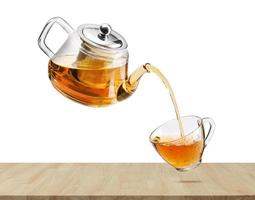 Jug pouring hot tea into glass cup with flying whirl green tea leaves in the air, Healthy products by organic natural ingredients concept, Empty space in studio shot isolated on white background photo