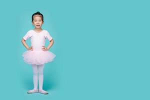 bella niña asiática sonriente con traje rosa está bailando un ballet en la escuela, espacio vacío en una foto de estudio aislada en un colorido fondo azul