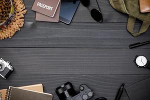 Traveler's accessories with passport, books of travel plan, wallet, camera, hat, backpack and airplane toy on black wooden table, Flat lay with copy space, Travel concept background photo