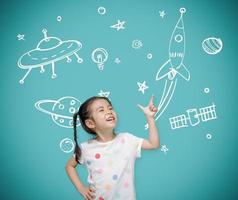 niña asiática apuntando a la pizarra con imaginación el astronauta y el cohete espacial, creativo y sueños del concepto de infancia foto