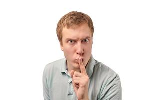 Funny guy in light gray Polo T-shirt asking to be quiet, silence gesture, white background photo