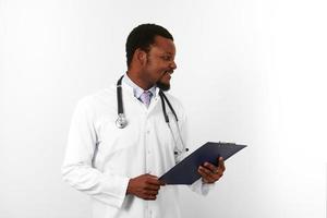 Smiling black bearded doctor man in white robe with stethoscope holds medical chart on clipboard photo