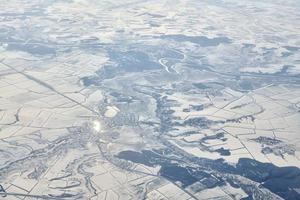 Aerial view over clouds top to snow covered rivers, fields and roads, winter fresh frosty air photo