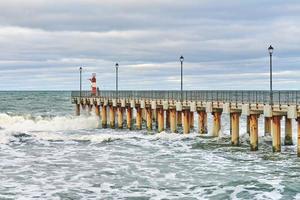 Fisherman in camouflage fishing on pier with lighthouse photo