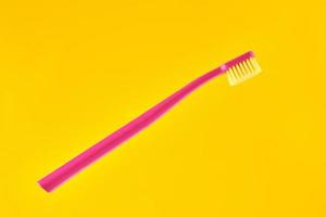Pink toothbrush on yellow background for oral hygiene to clean teeth, gums and tongue photo