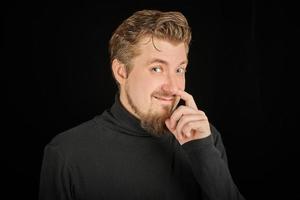 Funny bearded man picking his nose, black background photo