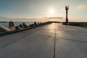 muelle norte con rompeolas, paisaje marino al atardecer. faro moderno a la luz del sol. tetrápodos a lo largo de los bordes del muelle. hermoso paisaje marino de noche. foto