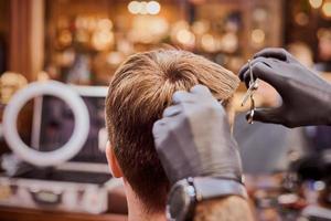 Male haircut in barbershop close up, client getting haircut by hairdresser with comb and scissors photo