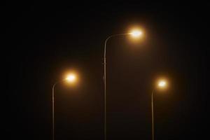 Three night lamppost shines with faint mysterious yellow light through evening fog at quiet night photo