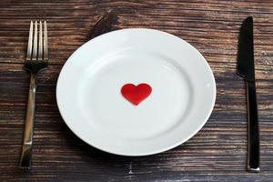 Waiting for a favorite dish in restaurant or cafe. Heart on plate with fork and knife. Lovers meeting at a daily lunch. photo