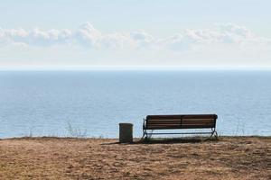 Empty bench with trashcan on cliff before sea background, peaceful quiet place for thinking alone photo