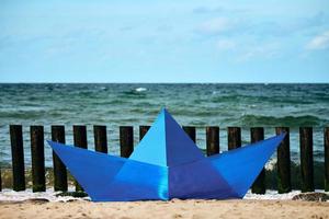 Origami blue paper boat on sandy beach for design, blue paper ship on sea shore. Beautiful horizon photo