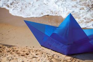 barco de papel azul de origami en la playa de arena para el diseño conceptual, hermoso barco de papel azul, primer plano foto