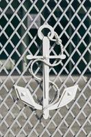 White anchor with mooring rope on mesh fence as symbol of navigation and maritime photo