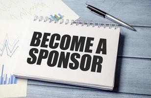 BECOME A SPONSOR text on blue wooden background and charts photo