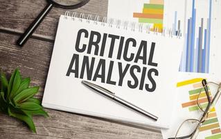 CRITICAL ANALYSIS words on notepad with magnifying glass and charts photo