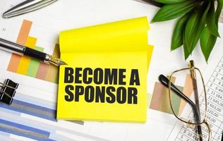 BECOME A SPONSOR text on the yellow paper with pen and glasses photo