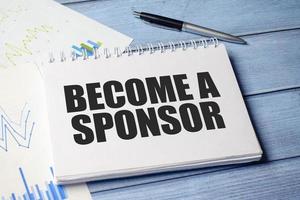 BECOME A SPONSOR text on blue wooden background and charts photo