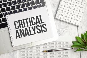 CRITICAL ANALYSIS text and notepad with pen, charts and calculator photo