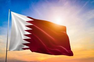 bandera de qatar ondeando y revoloteando en un espectacular sol que brilla a través del fondo de las nubes foto