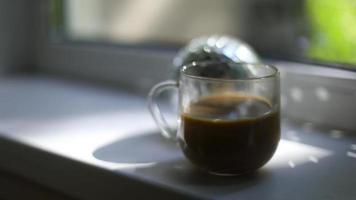 Cup of coffee on window. Morning coffee in light from window. Drink on windowsill. Transparent cup. video