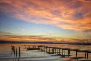 magnífica puesta de sol a la orilla del mar con muelle de madera y barco. foto