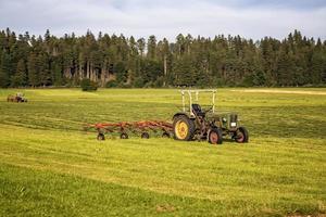 Agricultural machinery, a tractor collecting grass in a field against a blue sky. Season harvesting, grass, agricultural land. Selective focus photo