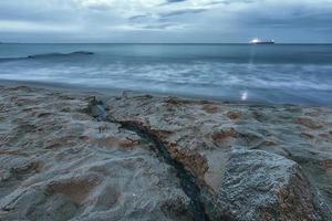 Amazing seascape with a light ray from the ship and a small brook flowing into the sea photo