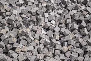 Pile of natural stone cubes for making outdoor pavement tiles. Chaotic stack of road tiles. Stone blocks. photo