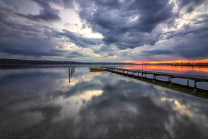 magnífica puesta de sol a la orilla del mar con muelle de madera y barco. foto